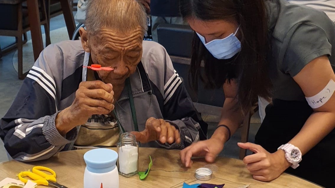 Hope (right) finds the most joy in engaging with patients at HCA Hospice as part of Havenue, a regular volunteering programme at NUS CSC. In the photo, she is helping Uncle Yong Hen, a patient at HCA Hospice, with an art project. (Photo: HCA Hospice)